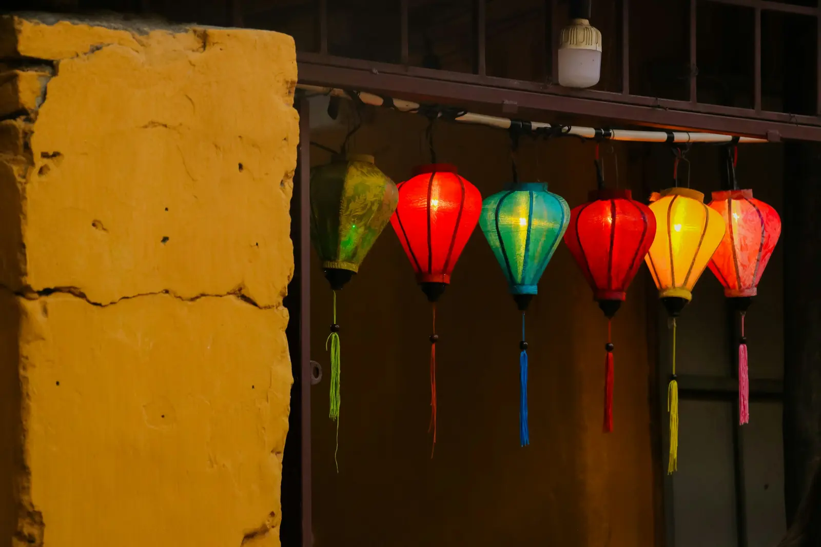 Colourful lanterns hanging against a yellow wall in Hoi An.