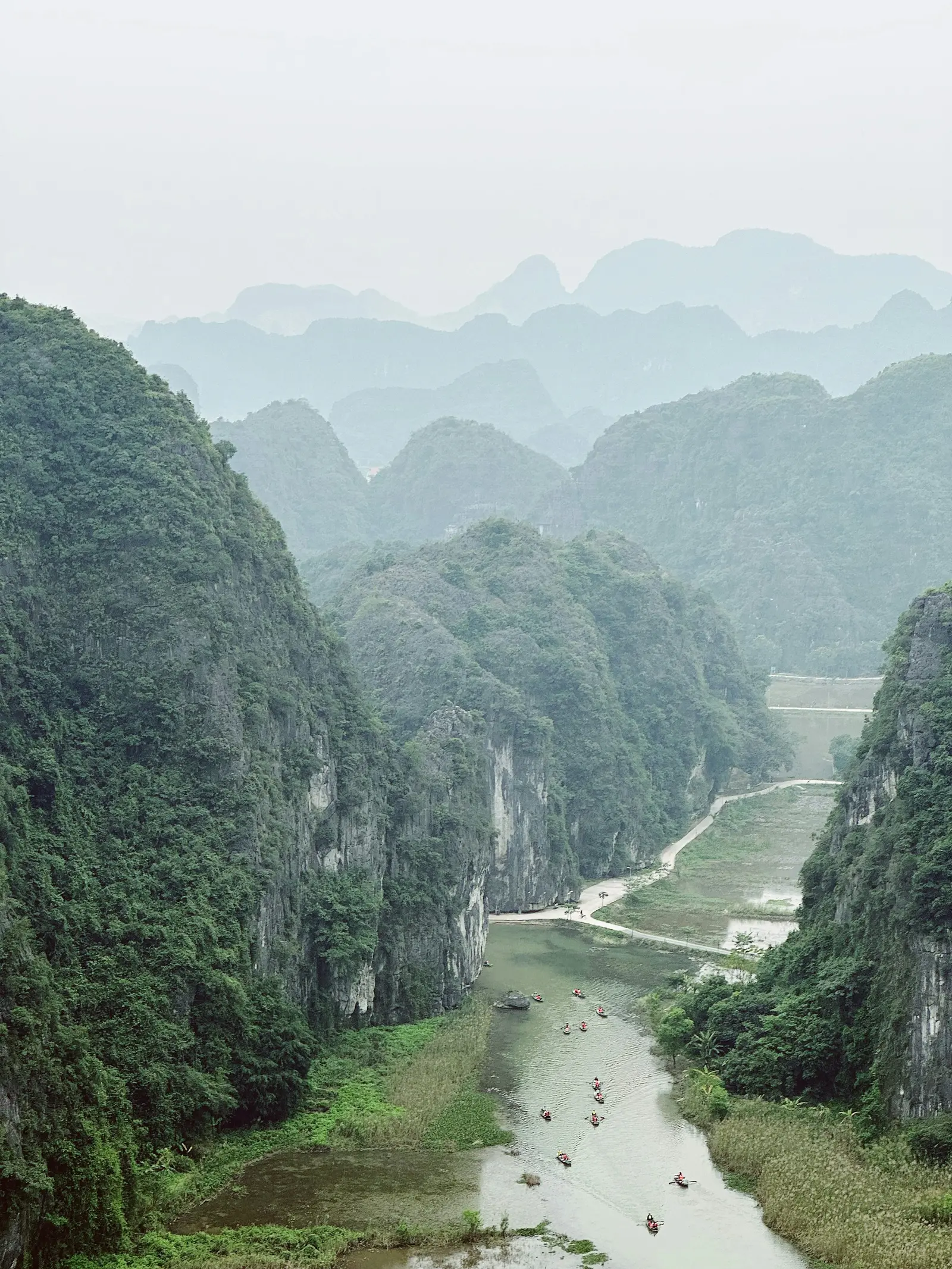 Boats on a river between green limestone mountains in Ninh Binh, Vietnam.